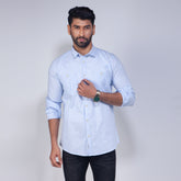 Man wearing a light blue shirt with rolled-up sleeves on a plain background