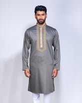 A man modeling a gray long-sleeve kurta with gold embroidery on the chest and cuffs, paired with white trousers, against a light gray studio background.