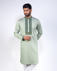 A man modeling a sage green long-sleeve kurta with detailed embroidery around the collar and chest, paired with white trousers, against a plain white studio background.