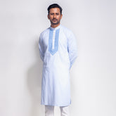 Man wearing a light blue embroidered panjabi with white pants on a plain background