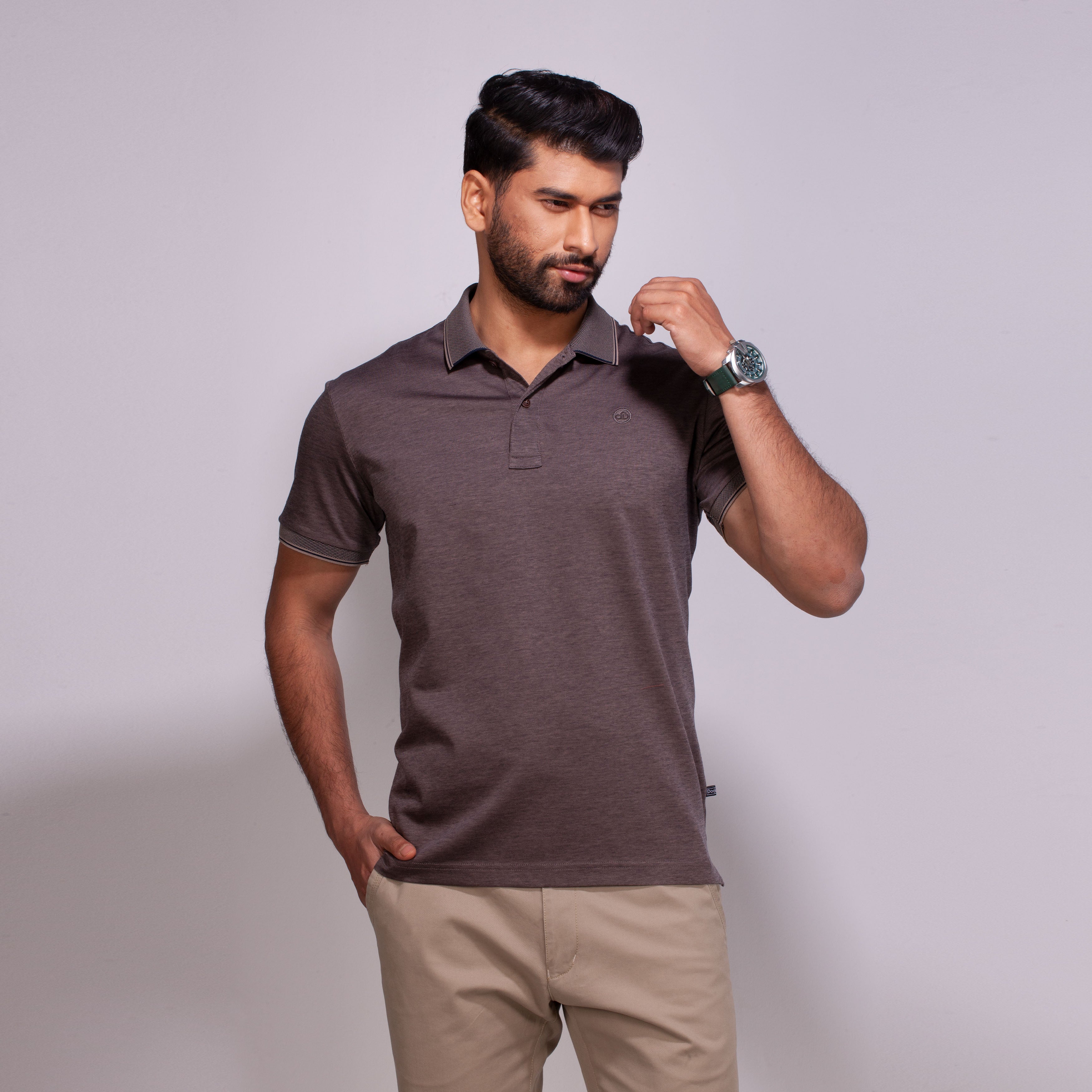 Man wearing a brown polo shirt and beige pants against a plain background