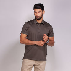 Man wearing a brown polo shirt and beige pants against a light gray background