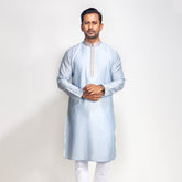 Man wearing a light blue kurta with white pants on a plain background