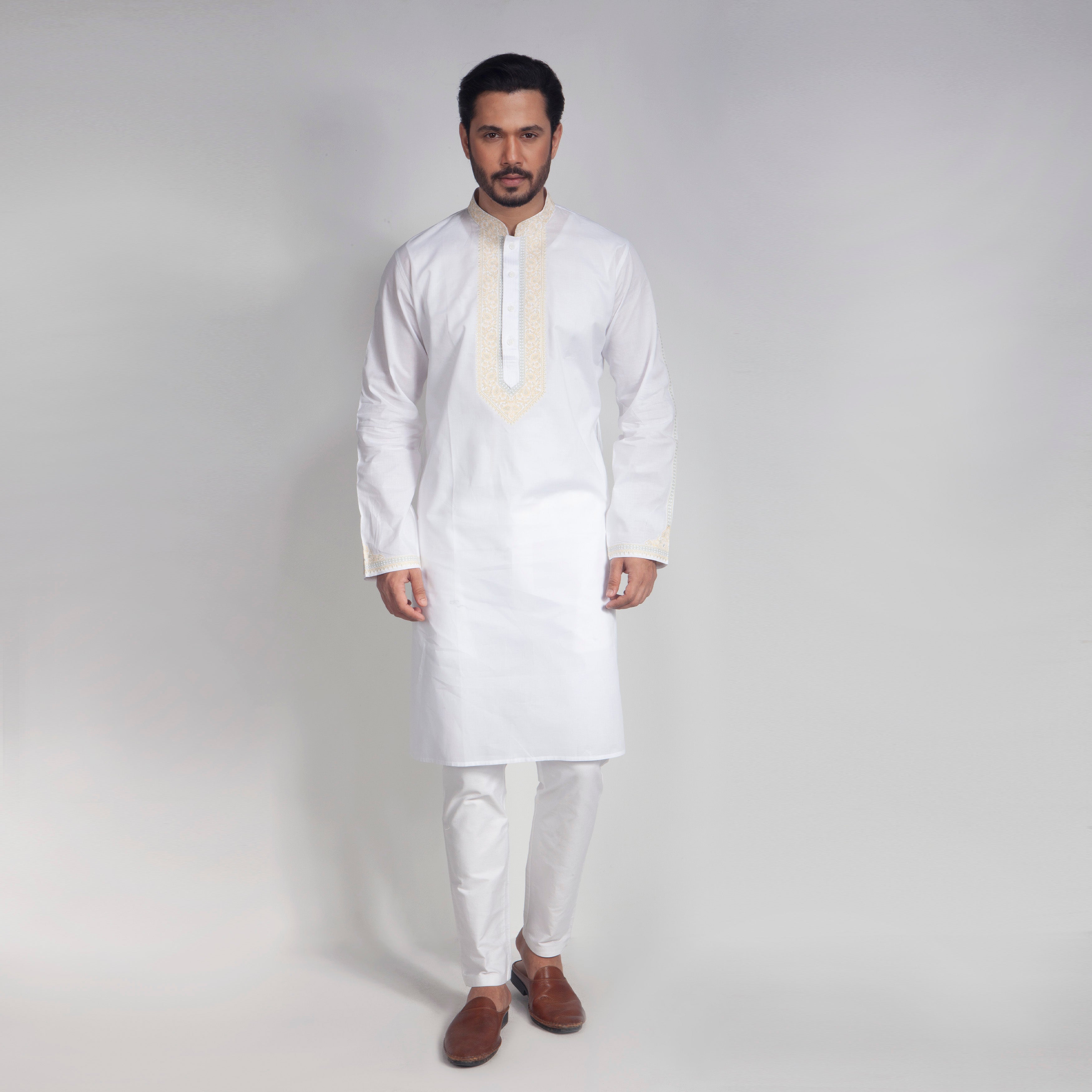 Man wearing a white kurta with embroidery on a plain background