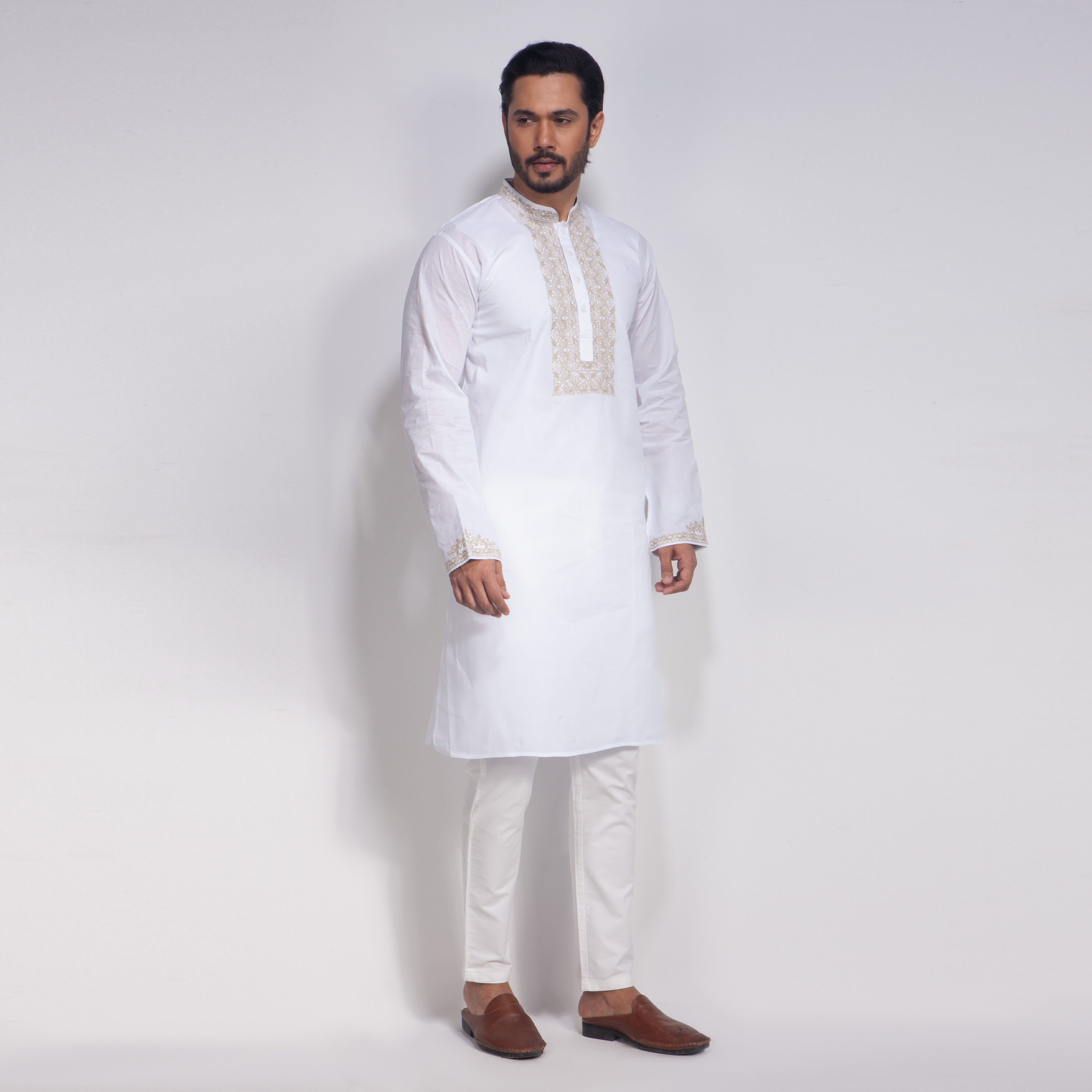 Man wearing a white kurta with embroidery on a plain background