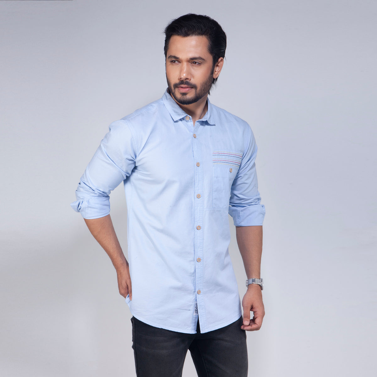 Man wearing a light blue shirt with rolled-up sleeves on a plain background