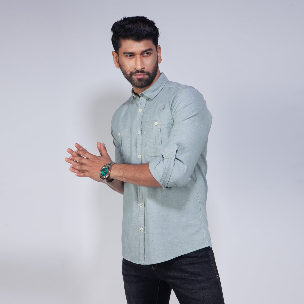 Man wearing a light gray shirt with rolled-up sleeves against a white background