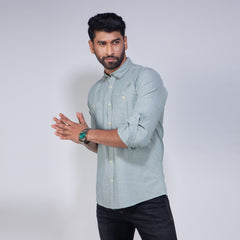 Man wearing a light gray shirt with rolled-up sleeves against a white background