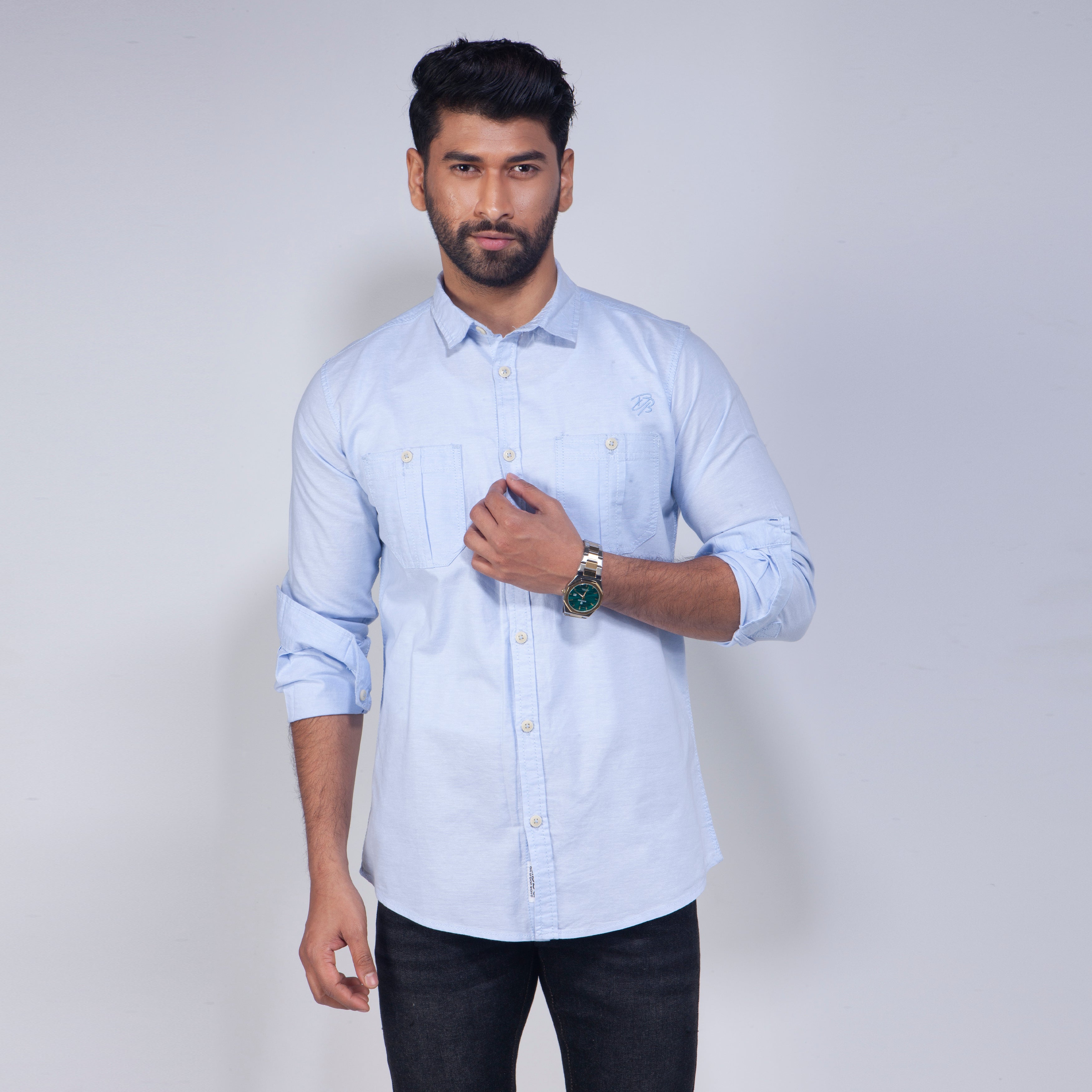 Man wearing a light blue shirt with rolled-up sleeves on a plain background