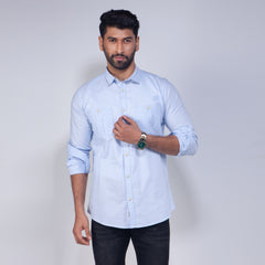 Man wearing a light blue shirt with rolled-up sleeves on a plain background