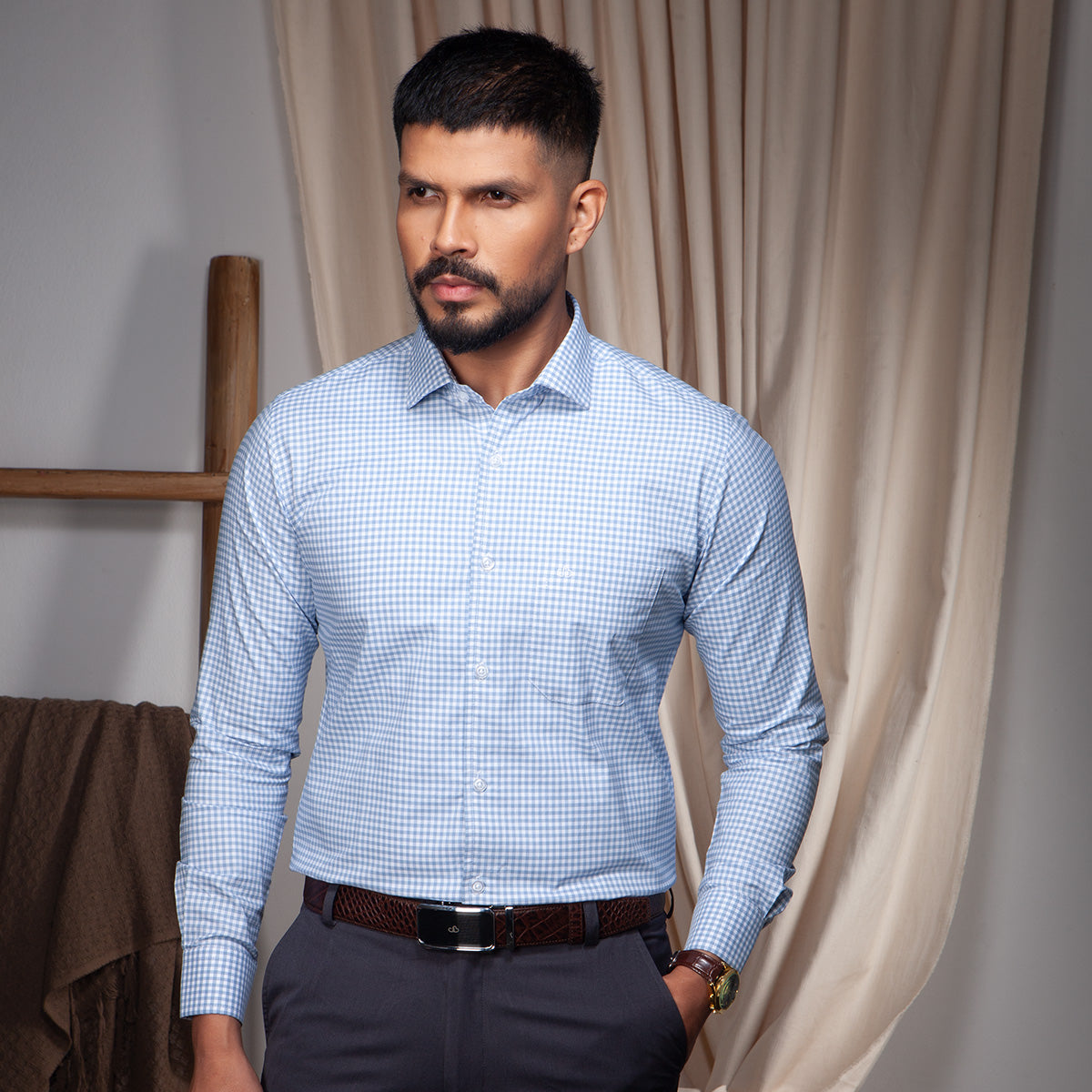 Man wearing a blue checkered formal shirt standing against a neutral background