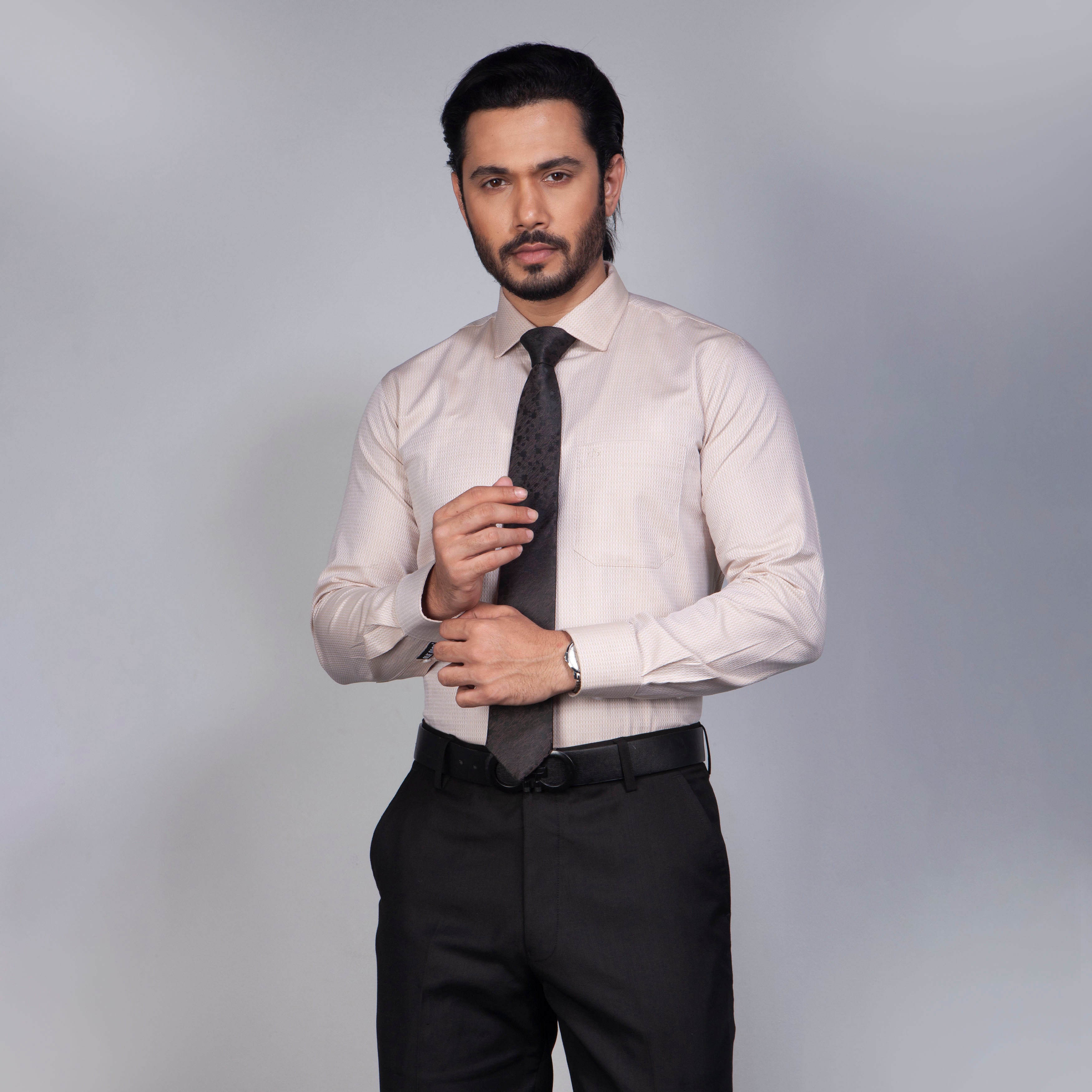 Man wearing a light-colored dress shirt, dark tie, and black pants against a gray background