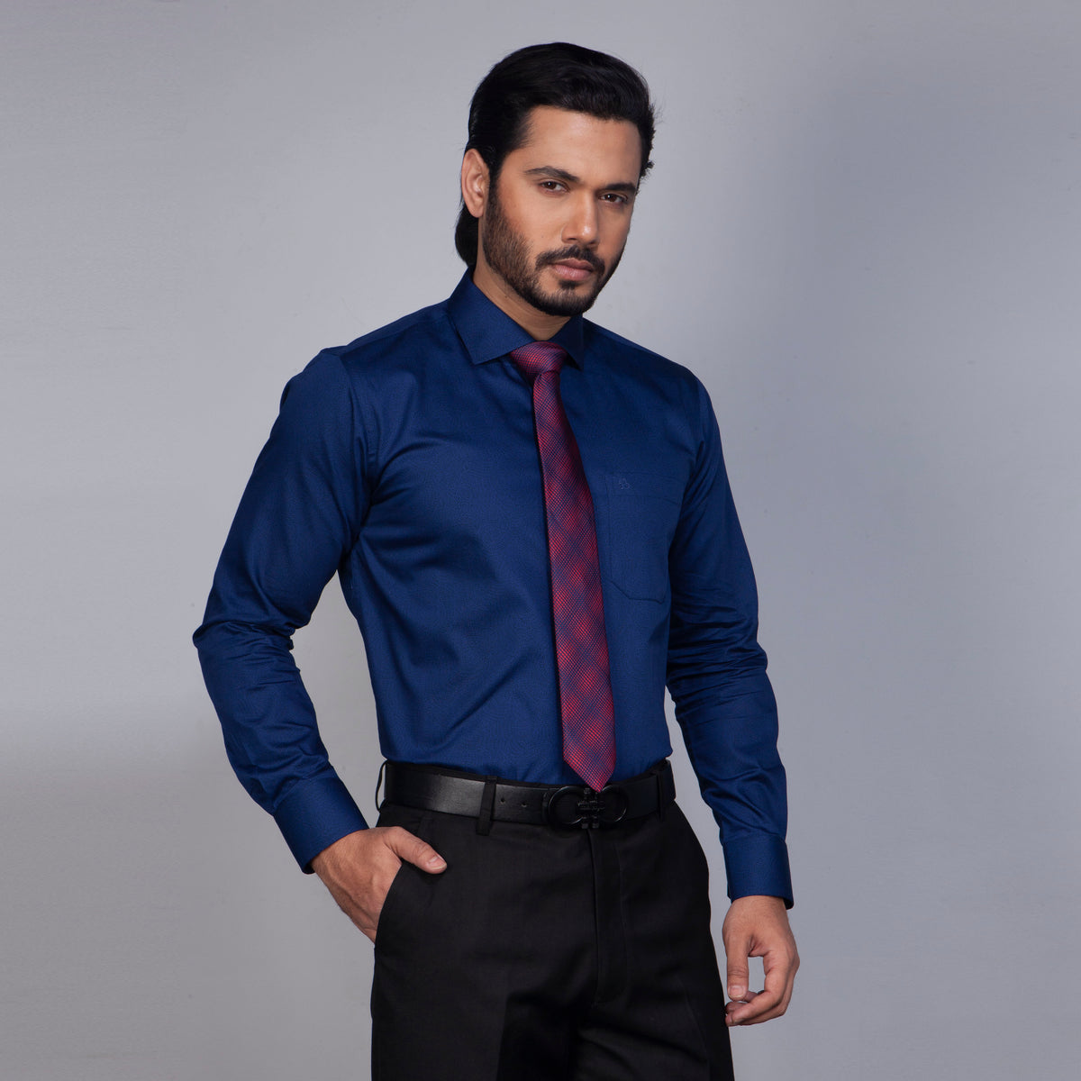 Man wearing a blue dress shirt with a red tie against a gray background