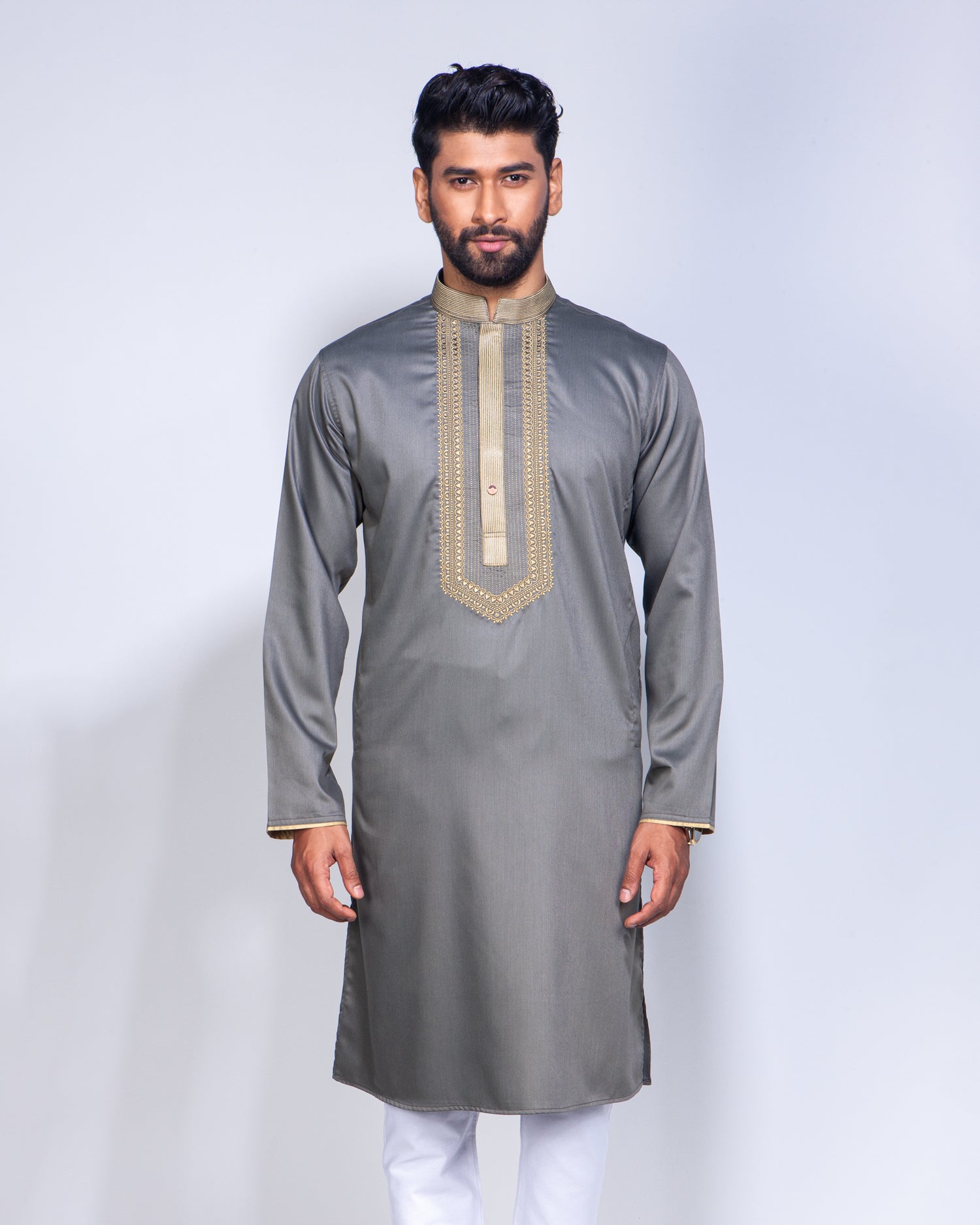 A man modeling a gray long-sleeve kurta with gold embroidery on the chest and cuffs, paired with white trousers, against a light gray studio background.