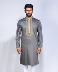 A man modeling a gray long-sleeve kurta with gold embroidery on the chest and cuffs, paired with white trousers, against a light gray studio background.