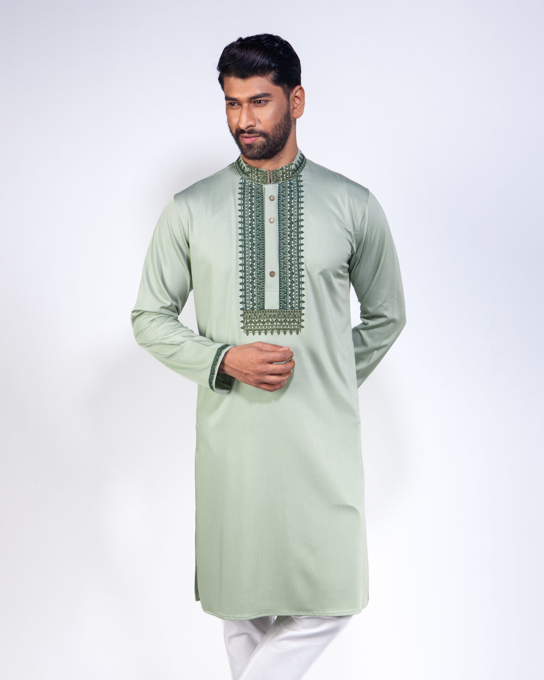 A man modeling a sage green long-sleeve kurta with detailed embroidery around the collar and chest, paired with white trousers, against a plain white studio background.