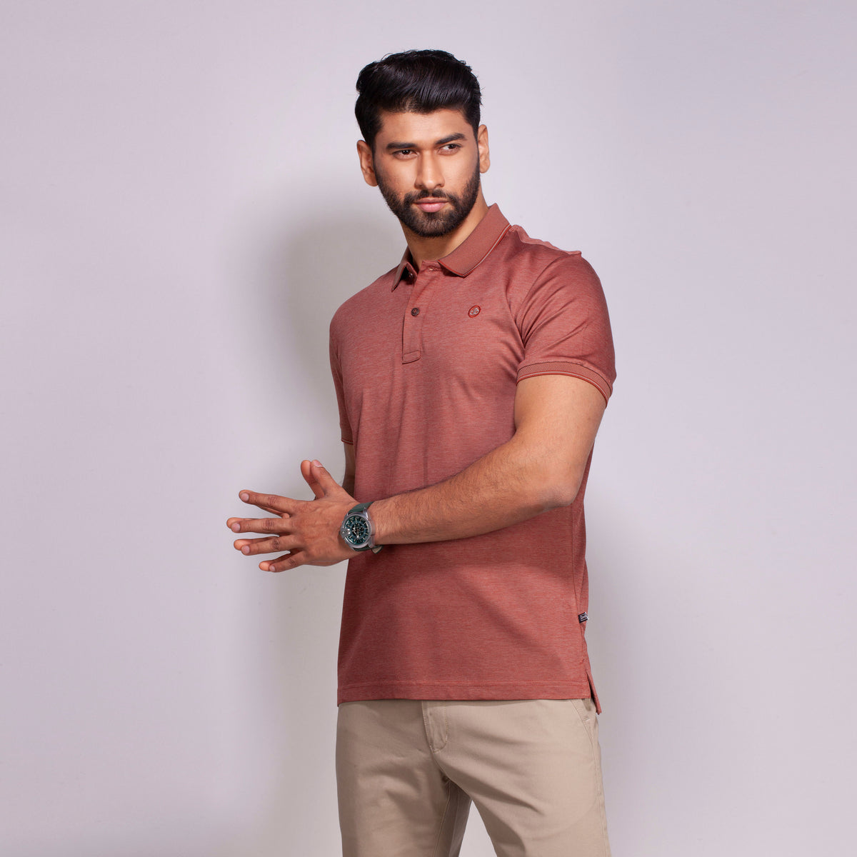 Man wearing a maroon polo shirt and beige pants against a light gray background