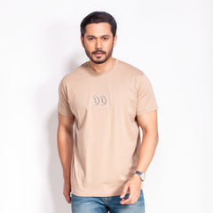 Man wearing a beige t-shirt with a logo on a white background