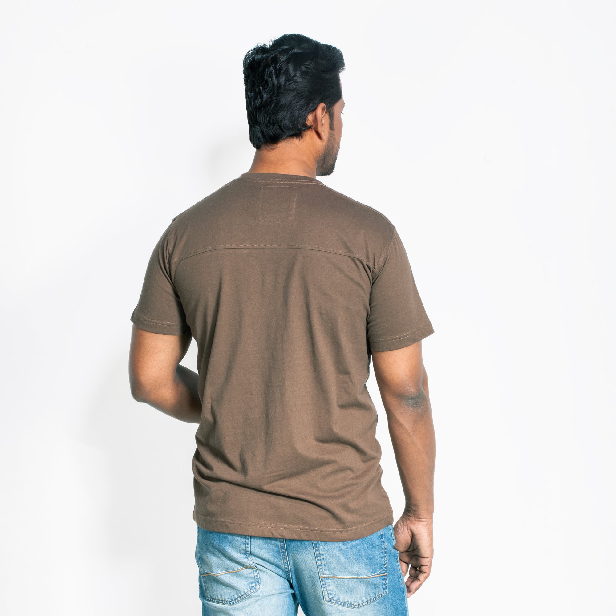 Man wearing a brown t-shirt and blue jeans on a white background
