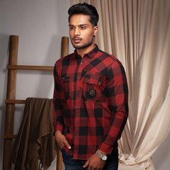 Man wearing a red and black plaid casual shirt standing in a room with a wooden ladder and draped fabric.