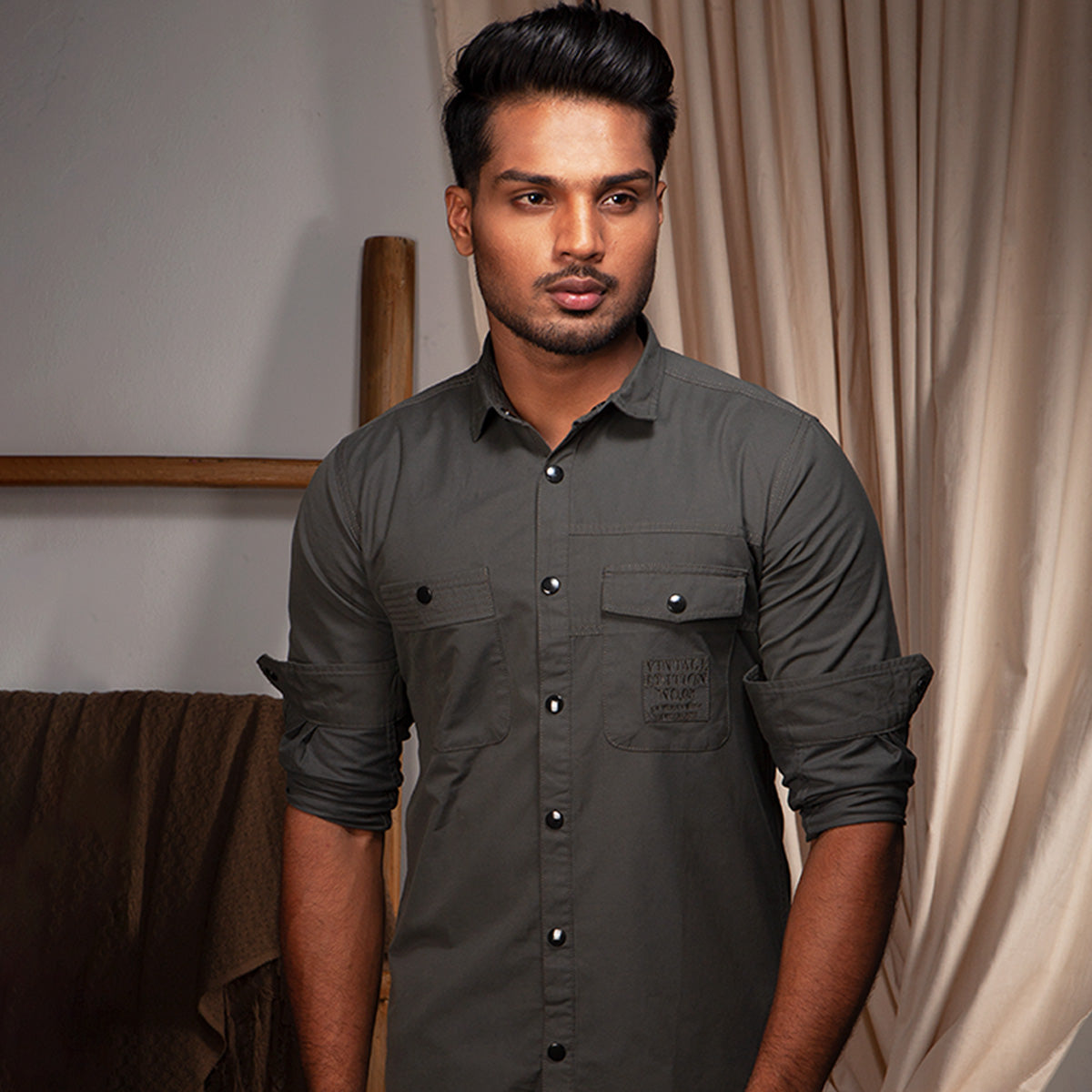 Man wearing a dark gray shirt standing indoors with neutral background