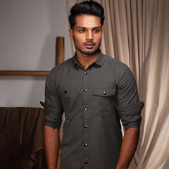 Man wearing a dark gray shirt standing indoors with neutral background