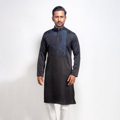 Man wearing a black kurta with white pants on a light gray background