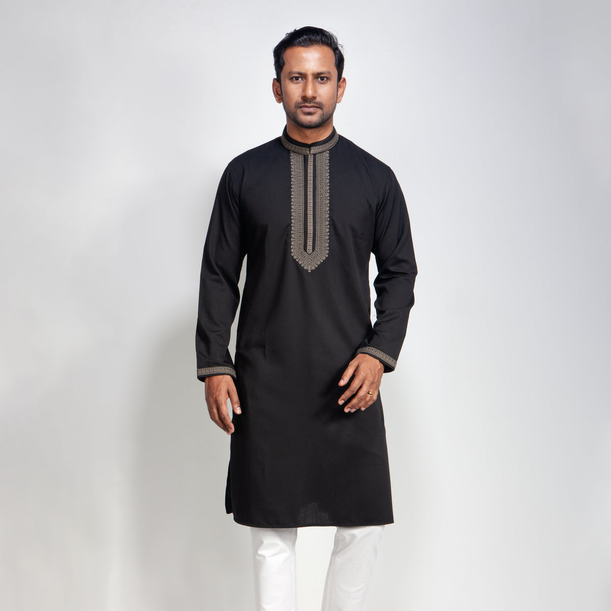 Man wearing a black embroidered panjabi with white pants on a light gray background