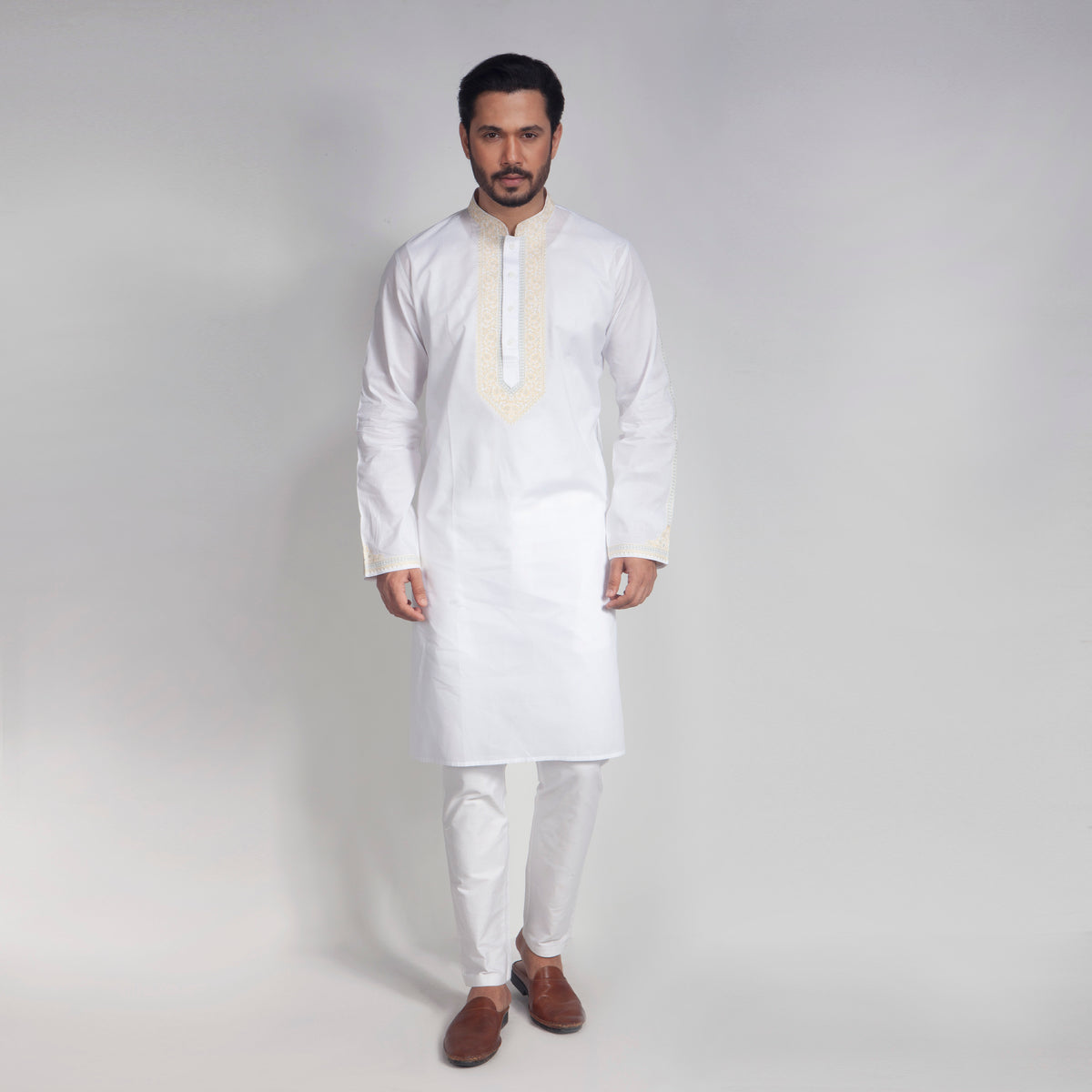 Man wearing a white kurta with embroidery on a plain background